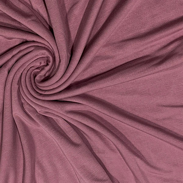 A close-up of draped dusty rose fabric arranged in a spiral pattern, showing its soft texture and color.