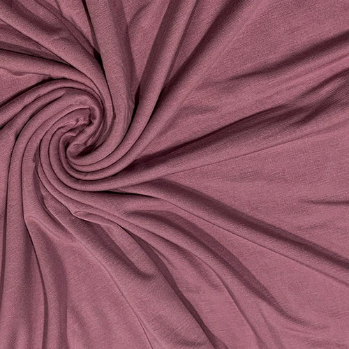 A close-up of draped dusty rose fabric arranged in a spiral pattern, showing its soft texture and color.