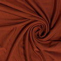 A close-up of draped rust-brown fabric arranged in a spiral, showing the material texture and color.