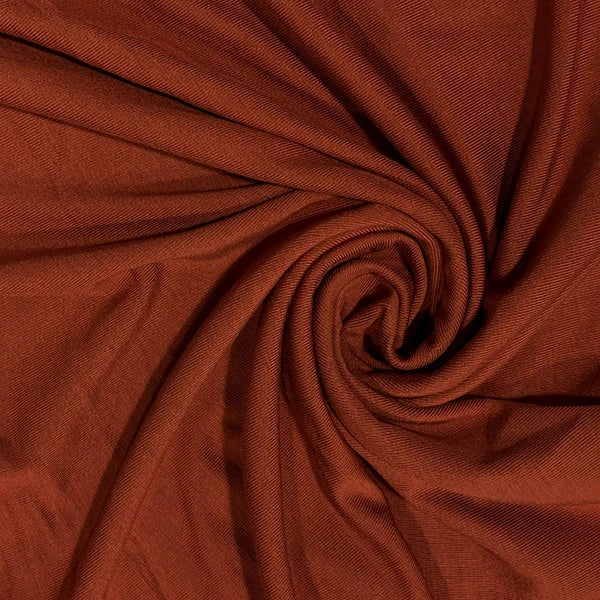 A close-up of draped rust-brown fabric arranged in a spiral, showing the material texture and color.