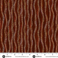 A close-up of a fabric pattern featuring vertical wavy lines in dark brown, rust red, and beige, decorated with dotted Aboriginal-style dot art. A white ruler with black markings and the brand name 'andover' is visible along the bottom edge.